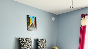 Ein Schlafzimmer mit Bett, Kissen, einem Nachttisch, einem Gemälde und einem Fenster mit Vorhängen.