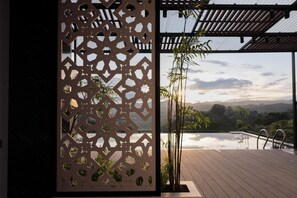 A modern outdoor deck with a wooden floor, a decorative metal partition, and a view of a mountainous landscape.