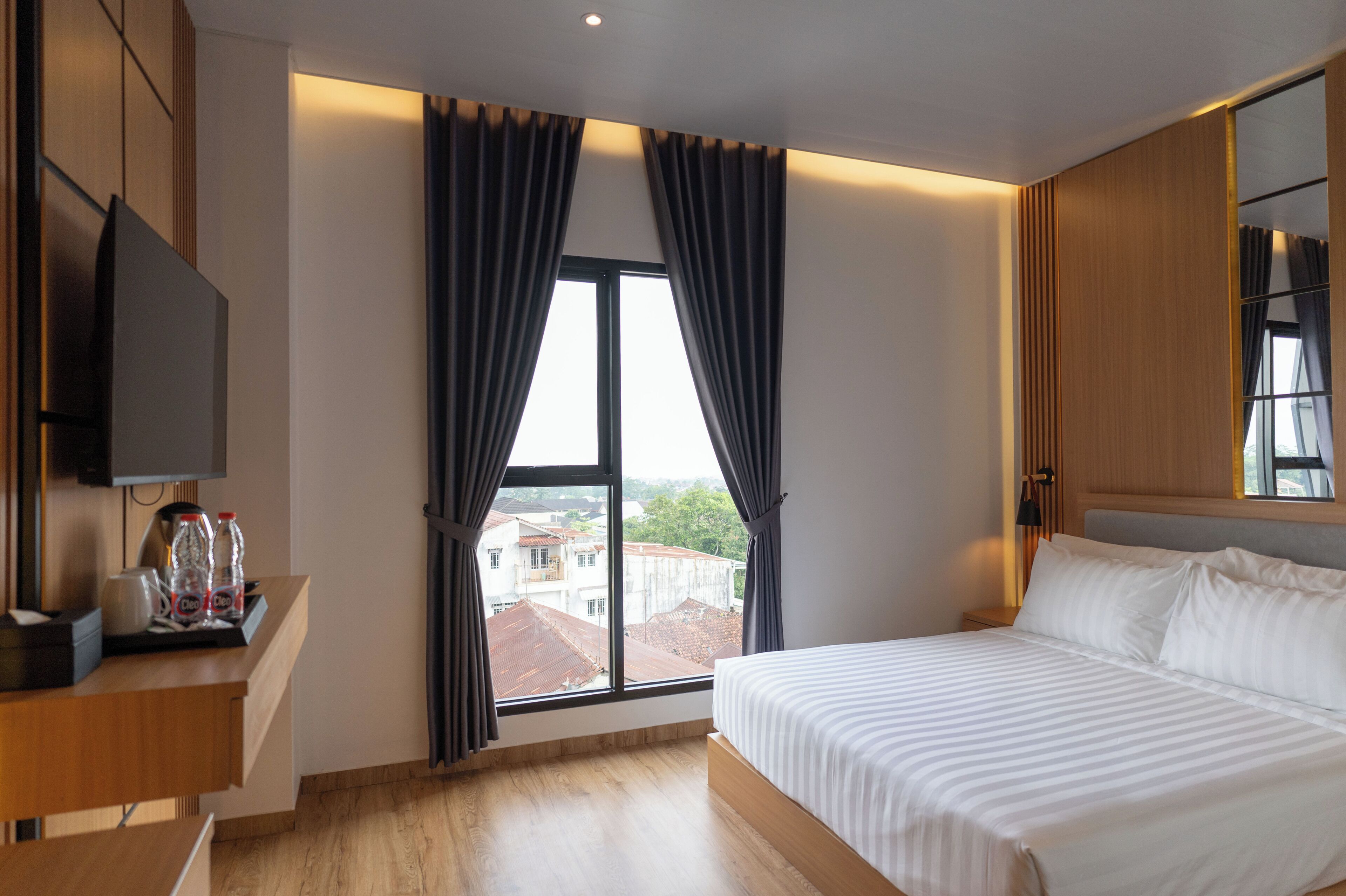 A modern hotel room with a large bed, a TV on a wooden desk, and a window with curtains.