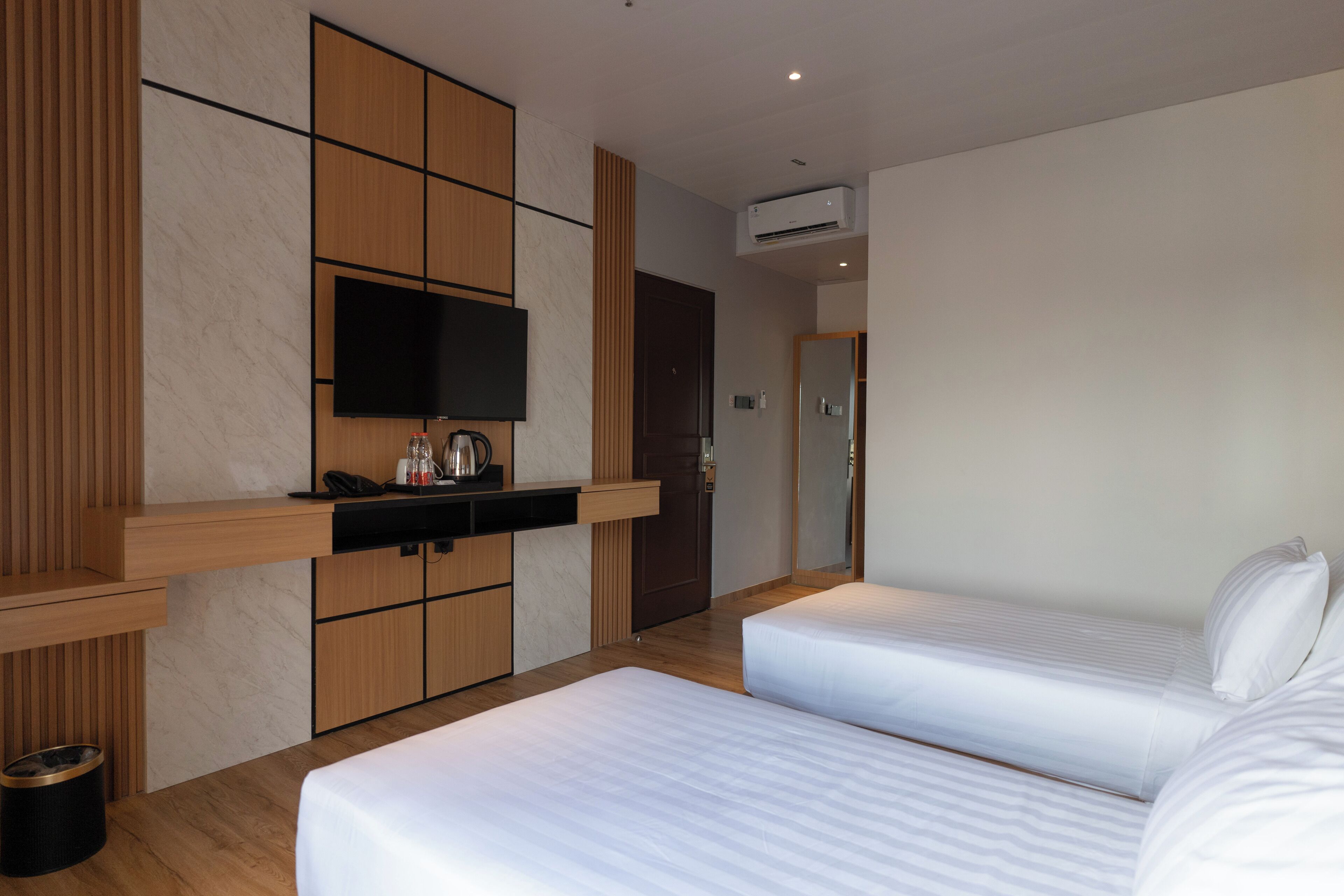 Una habitación de hotel moderna con dos camas, un televisor de pantalla plana, un minibar y un panel de pared de madera.