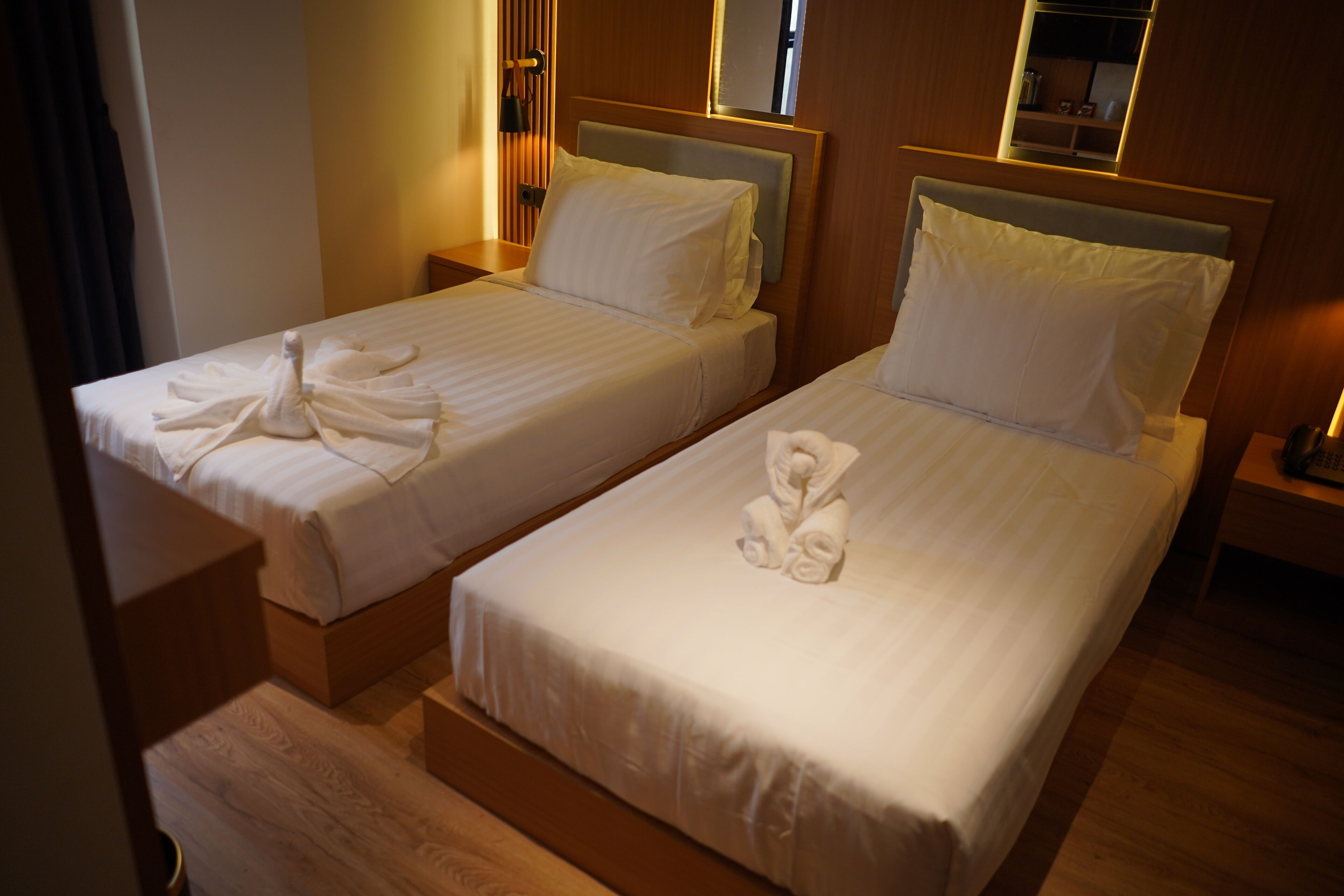 Two single beds with white linens and towels, wooden headboards, and bedside tables.