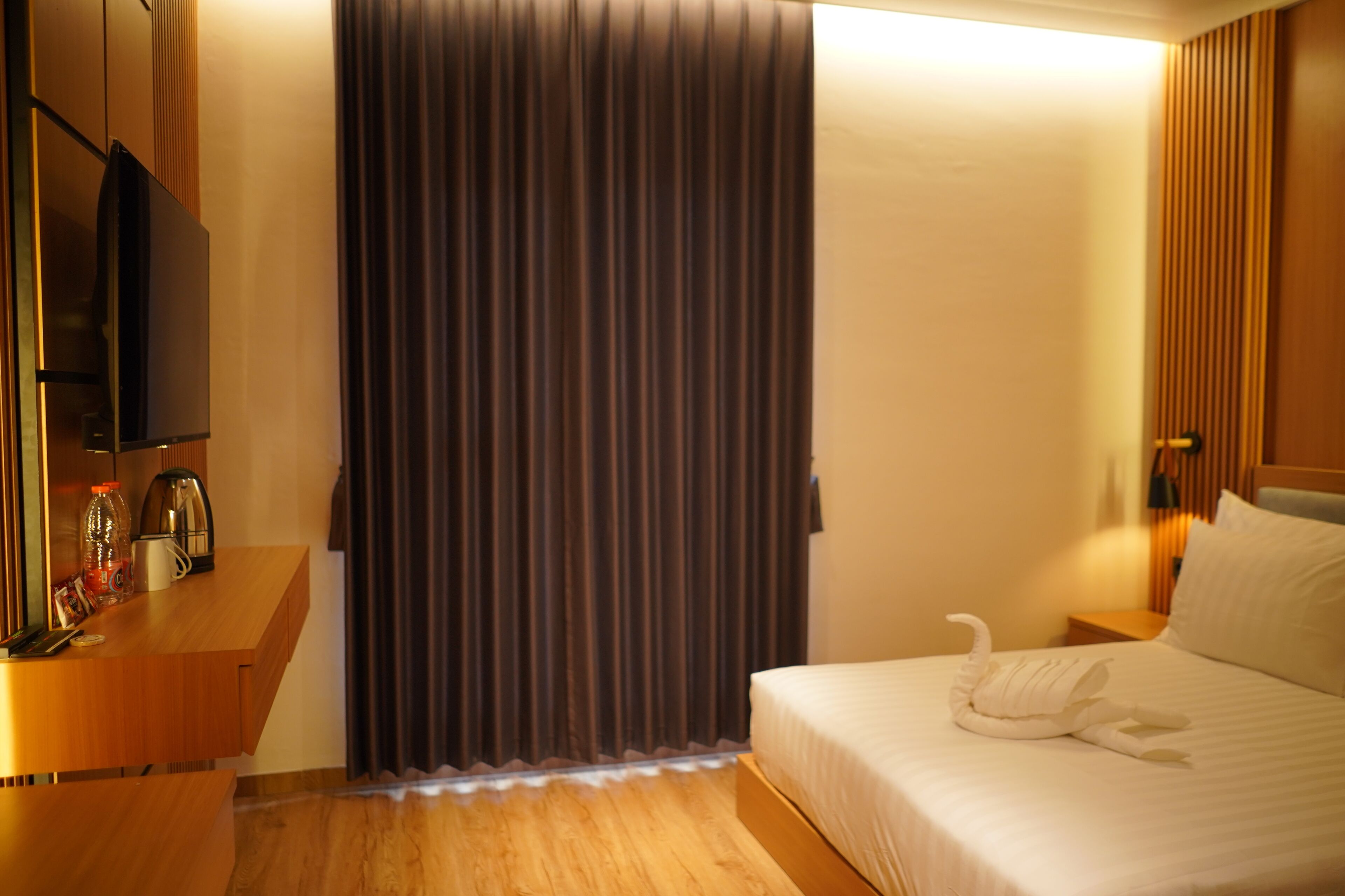 Quarto de hotel com cama, televisão, escrivaninha de madeira, cafeteira e cortina.