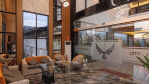 A modern lobby with wicker furniture, a marble floor, and a large window with a city view. - Eagle Hotel Wonosobo, Azana Hotels Collection (Wonosobo)