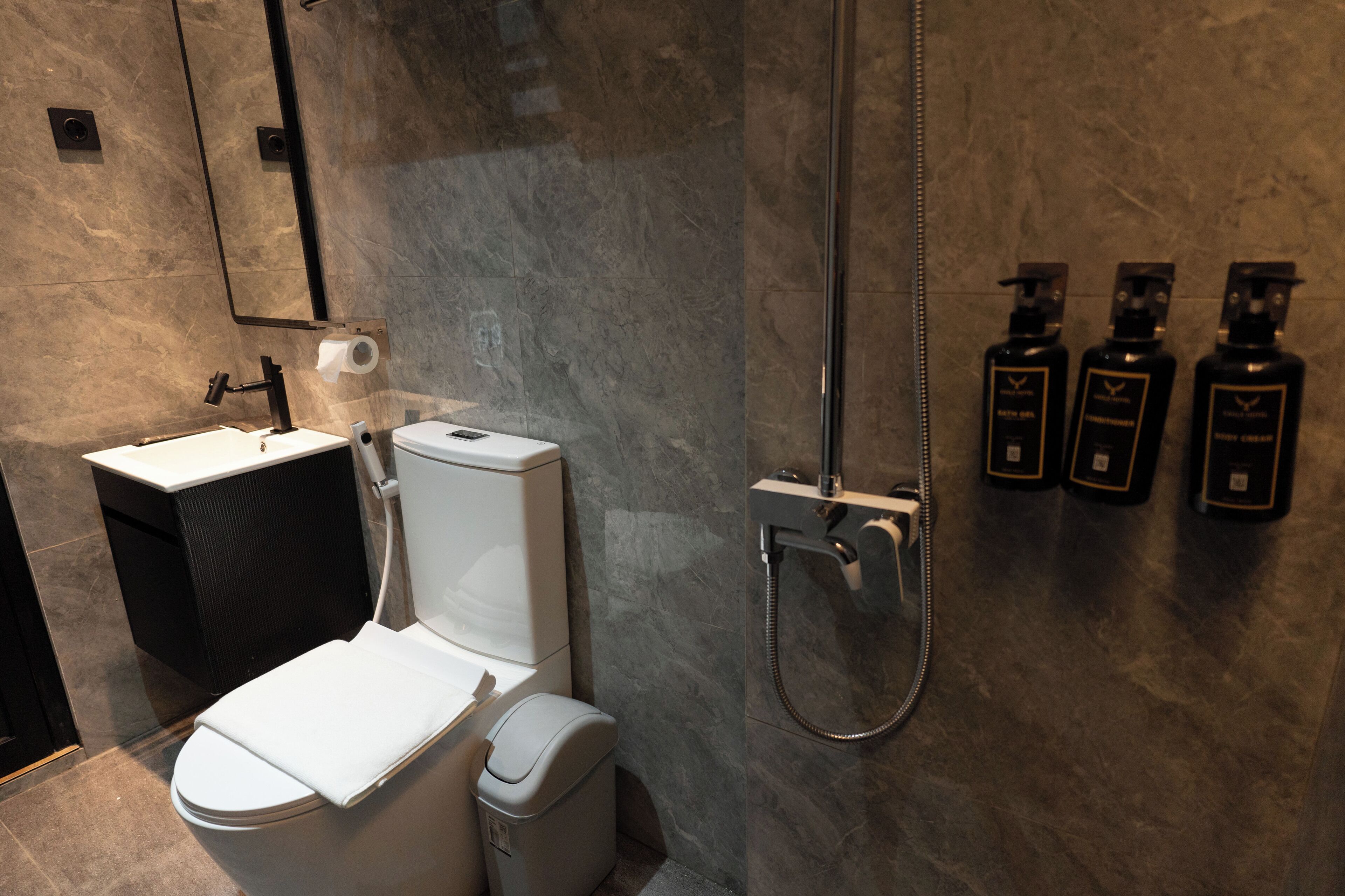A modern bathroom with a toilet, sink, and shower. There are three bottles of toiletries on the wall.