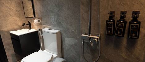 A modern bathroom with a toilet, sink, and shower. There are three bottles of toiletries on the wall.