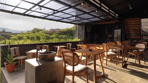 An outdoor patio with wooden furniture, a stone table, and a view of greenery and distant buildings. - Eagle Hotel Wonosobo, Azana Hotels Collection (Wonosobo)