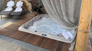 Un bain à remous doté d’un panneau de commande, entouré d’une terrasse en bois et d’un sol en pierre.