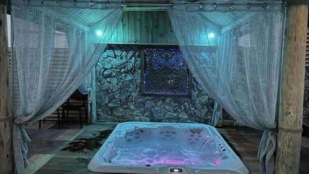 Un bain à remous dans une pièce rustique aux murs de pierre et au plancher de bois.