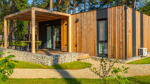 A modern wooden cabin with a covered patio, stone pathway, and green chairs. - Modern Chalet in a Holiday Park (Parc Hosingen)