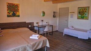 Una habitació d'hotel amb un llit gran, un llit més petit, un escriptori amb una cadira i dos quadres a les parets.