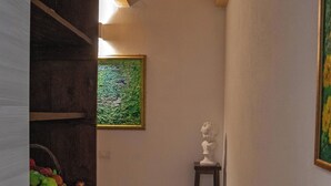 Un passadís estret amb bigues de fusta al sostre, una petita estàtua sobre un tamboret i un quadre verd amb textura a la paret.