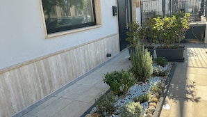Um edifício moderno com fachada limpa, uma janela e um pequeno jardim com diversas plantas e pedras.