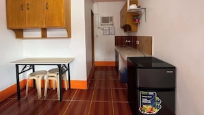Eine kompakte Küche mit Holzausstattung, einem schwarzen Kühlschrank, einem kleinen Tisch mit Stühlen und einem Fliesenboden.