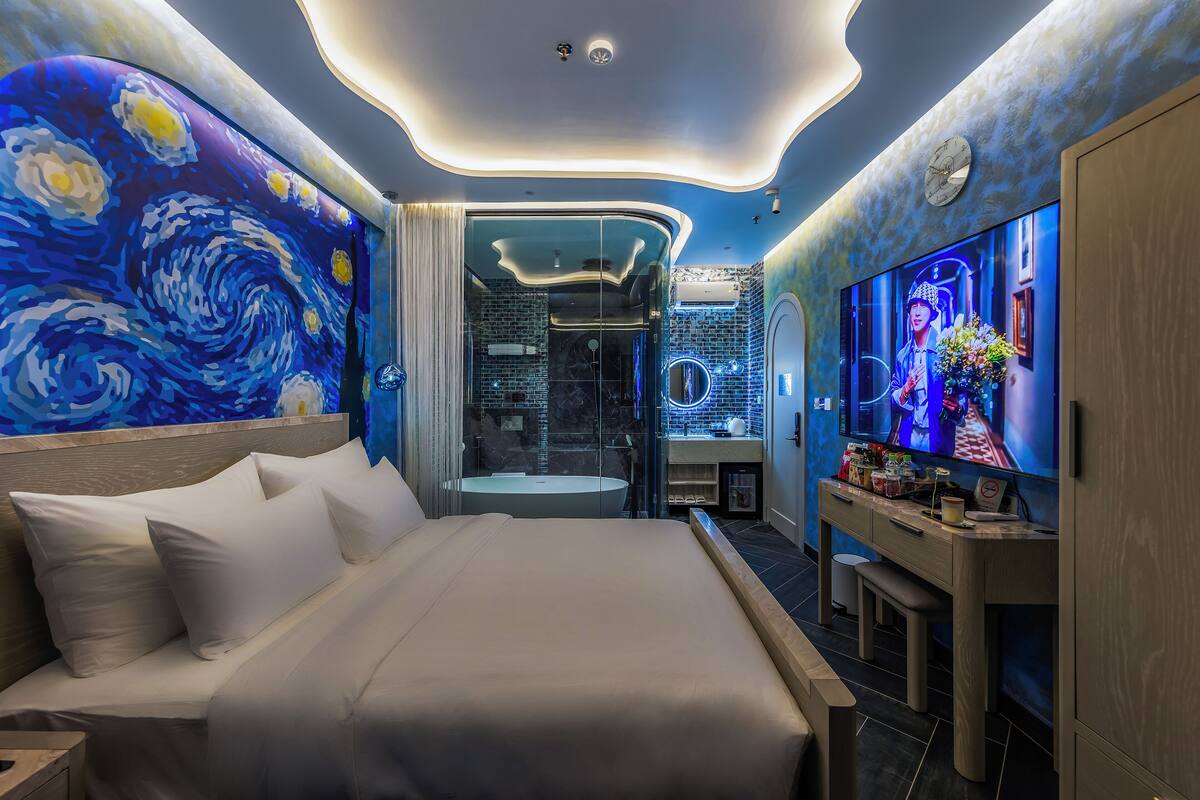 A modern bedroom with a large bed, a vanity with a mirror, and a television on the wall.