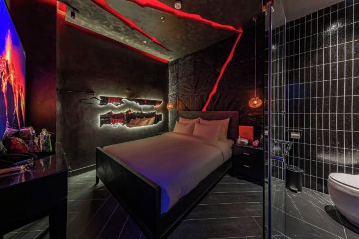 Un dormitorio moderno con cama, televisor montado en la pared y baño con inodoro y lavabo.