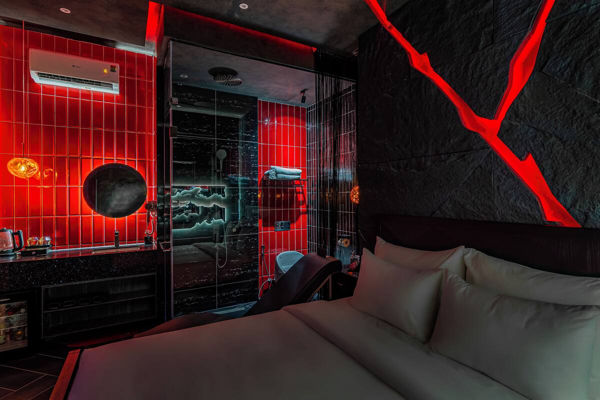 A modern hotel room with a large bed, a vanity with a mirror, and a red-lit shower area.