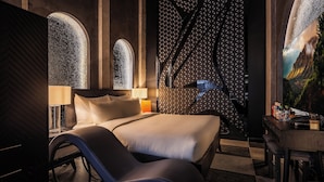 Quarto de hotel moderno com uma cama grande, uma escrivaninha e uma cadeira. Há uma janela com vista para montanhas e um quadro na parede.