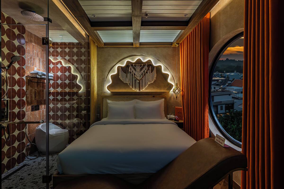 A modern hotel room with a large bed, a shower, and a view of the city through a window.