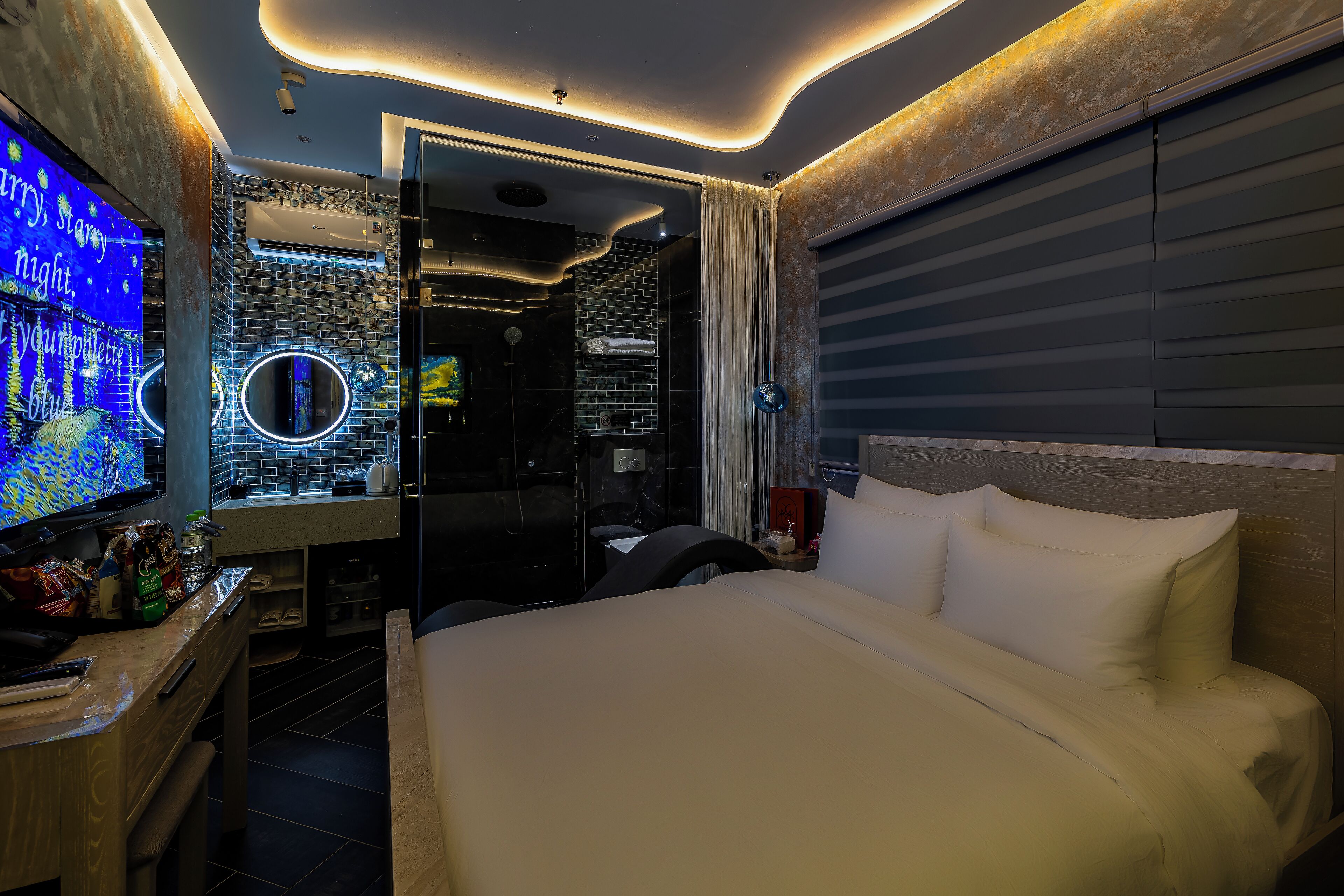 A modern hotel room with a large bed, a TV, a desk, and a bathroom visible through an open door.