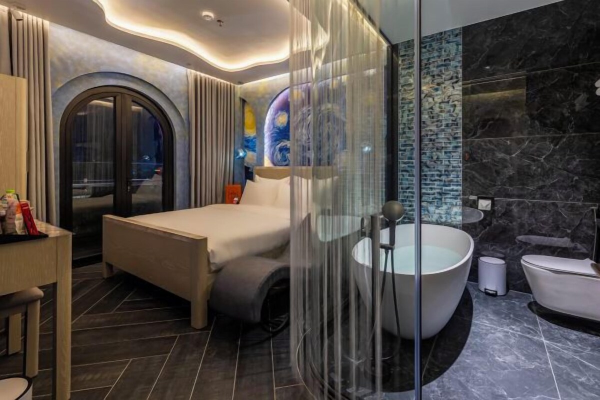 A modern bedroom with a large bed, a glass shower enclosure, and a marble-tiled bathroom.