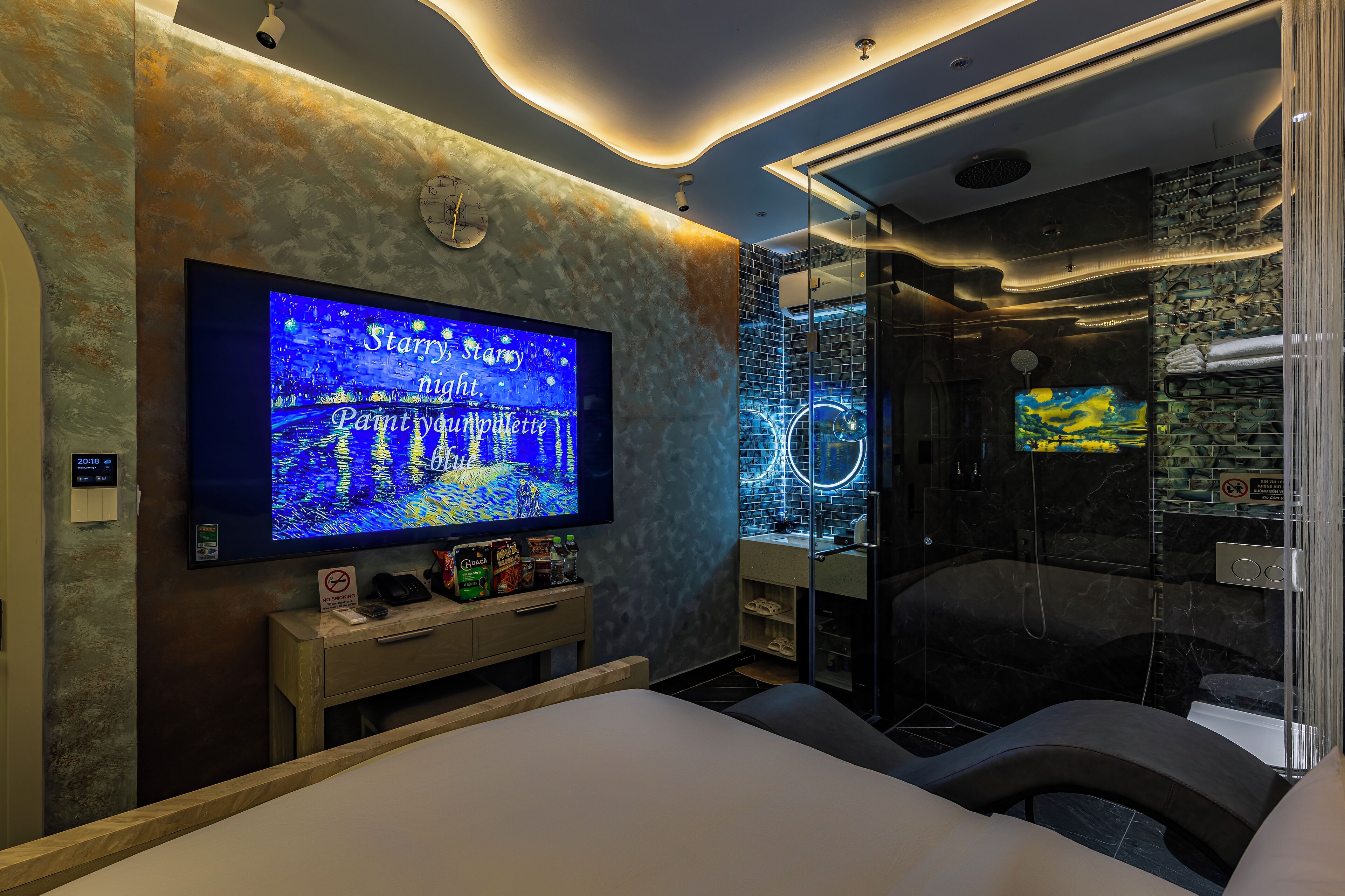 Una habitación de hotel moderna con un televisor de pantalla plana grande, cabina de ducha de vidrio y cama con cabecero.