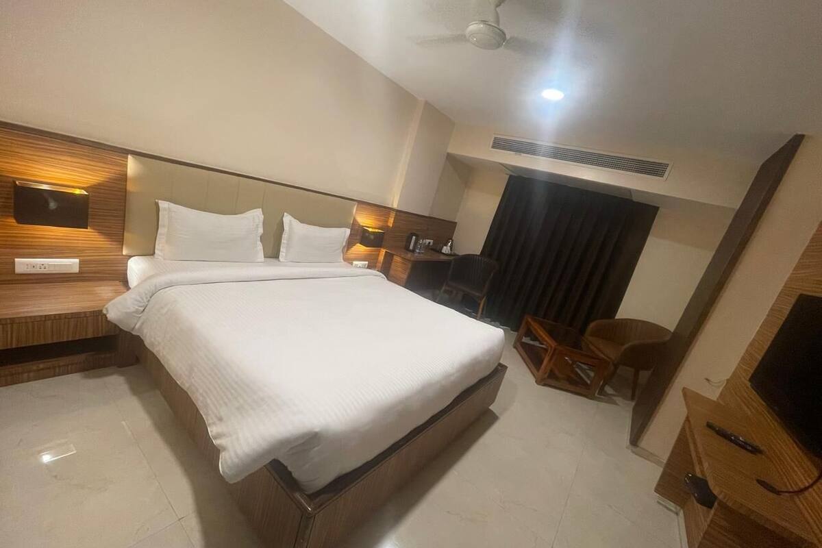 A hotel room with a large bed, a desk, a chair, a TV, and a ceiling fan.