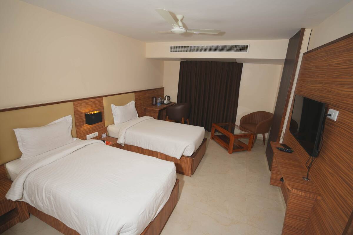 A hotel room with two beds, a desk, a chair, a television, and a ceiling fan.