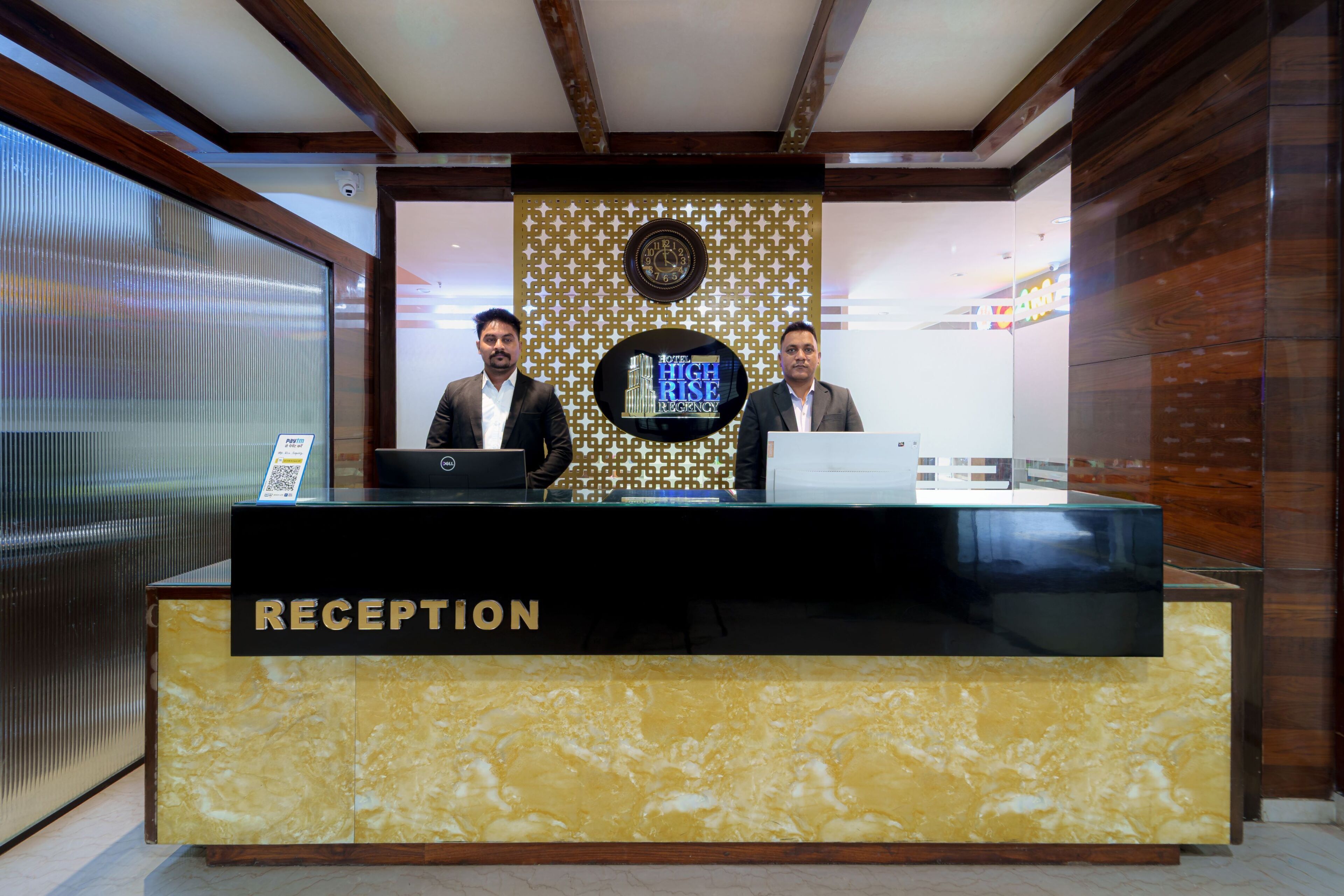 A reception desk with a 'RECEPTION' sign, two individuals behind it, and a clock on the wall.