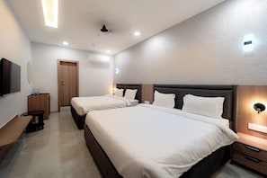 A modern hotel room with two beds, a wooden wardrobe, a small table, and a wall-mounted TV. - Hotel High Rise Regency (Burhanpur)