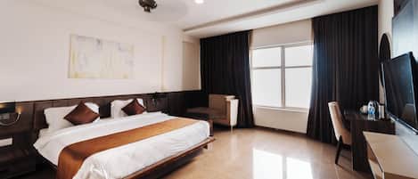 A hotel room with a large bed, a desk, a chair, a TV, and a window with curtains.