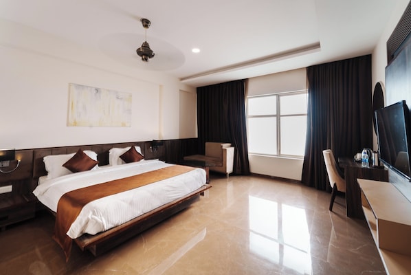A hotel room with a large bed, a desk, a chair, a TV, and a window with curtains.