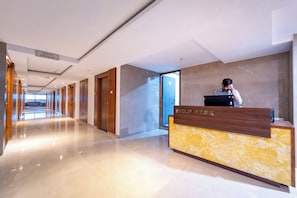 A hotel reception desk with a sign reading 'HELP DESK' and a person behind it. The hallway is lined with doors and has a polished floor.