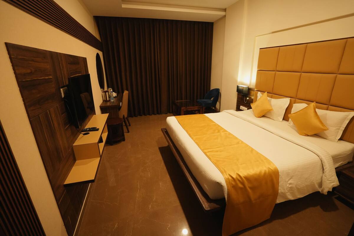A hotel room with a large bed, a desk, a chair, and a television.