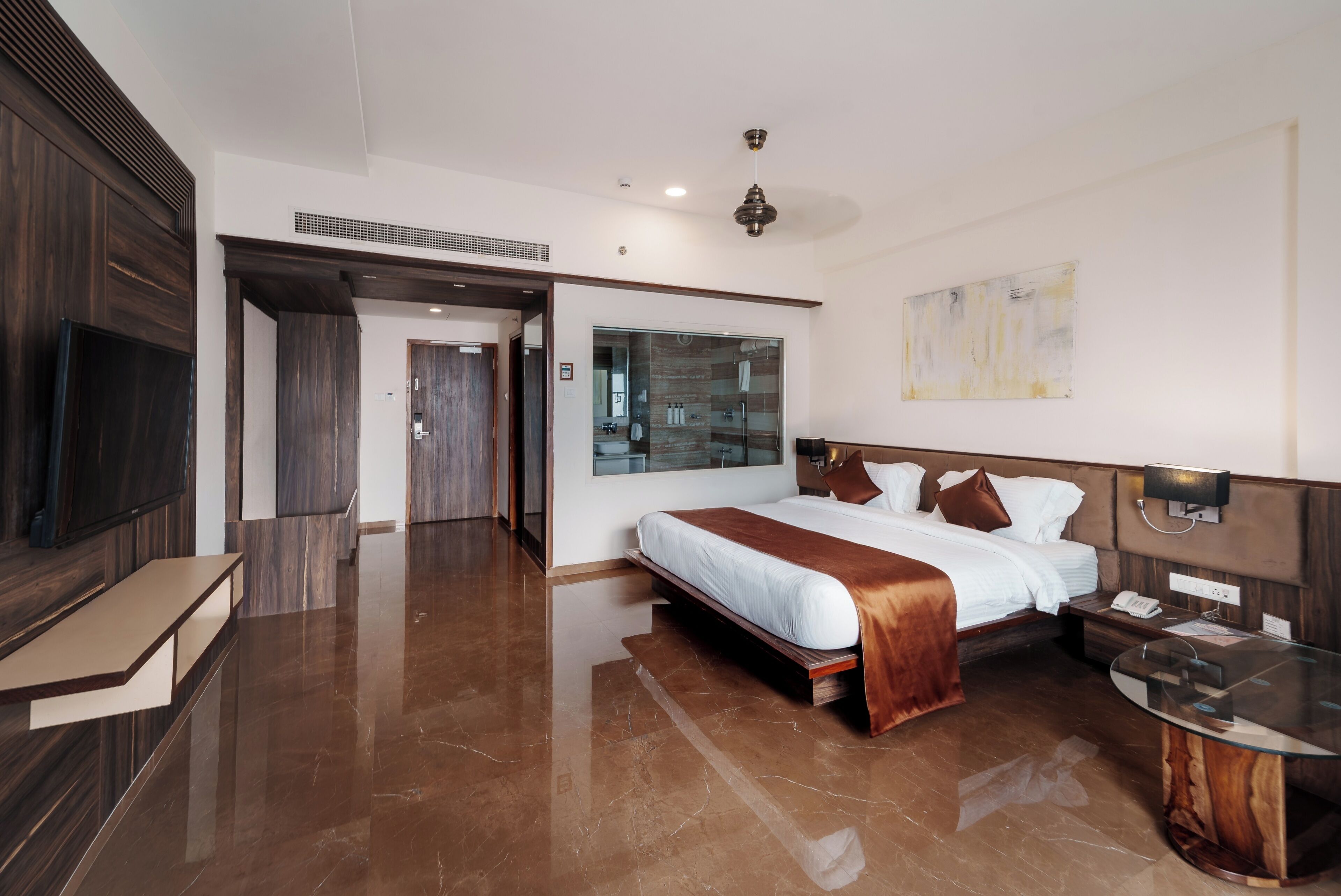 Een moderne hotelkamer met een groot bed, een bureau, een spiegel en een zichtbare badkamer achter een glazen deur.