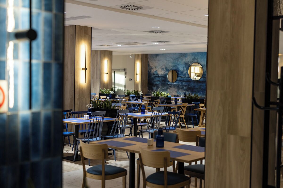 A modern dining area with multiple tables and chairs, wooden accents, and wall-mounted lighting.
