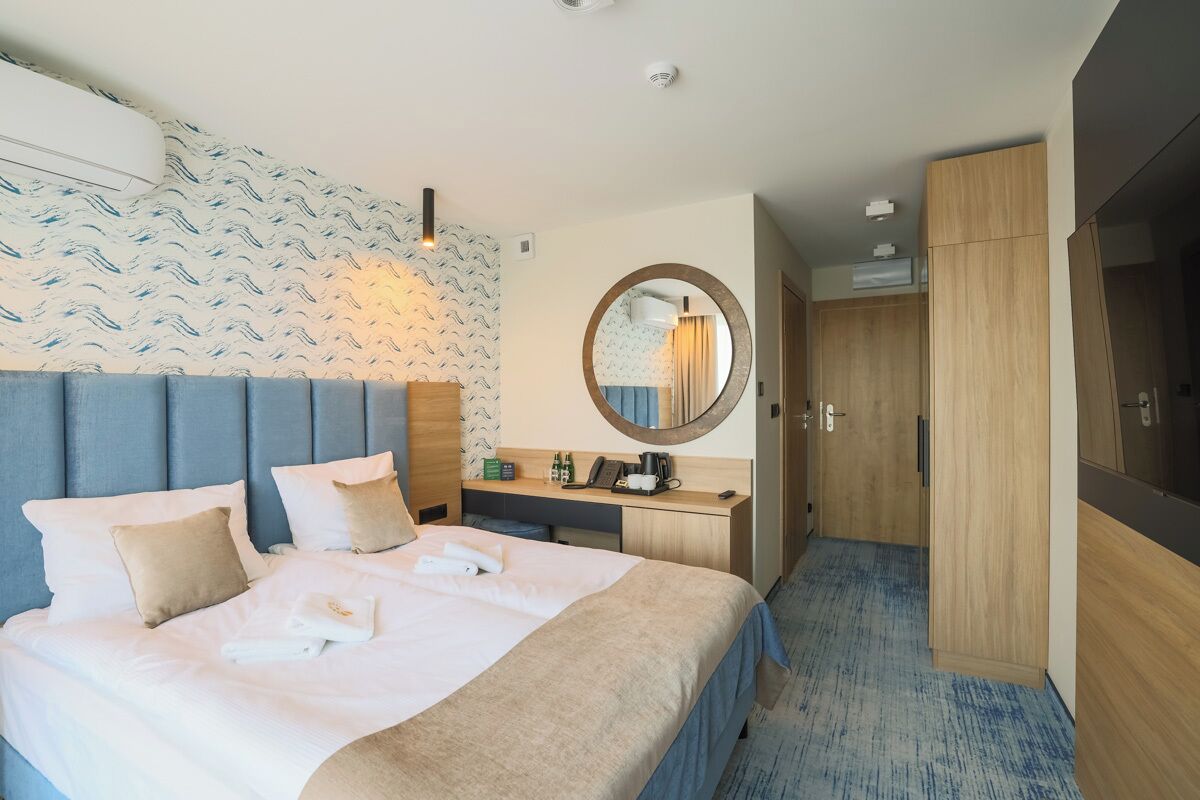 A hotel room with a bed, a desk, a mirror, and a wardrobe.