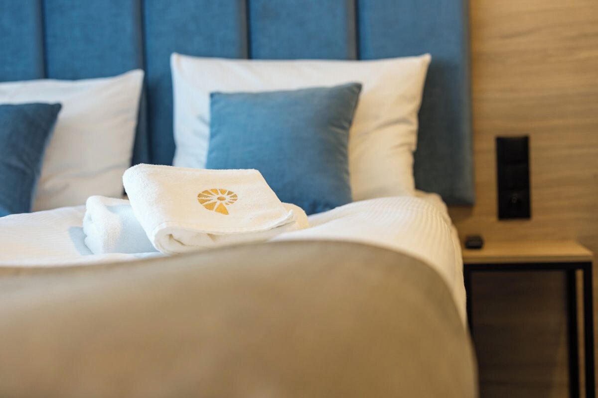 A neatly made bed with a white duvet and a towel with a logo on it.