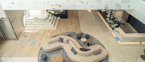 A modern lounge area with a curved sectional sofa, a round coffee table, and a glass ceiling with hanging decorative elements.