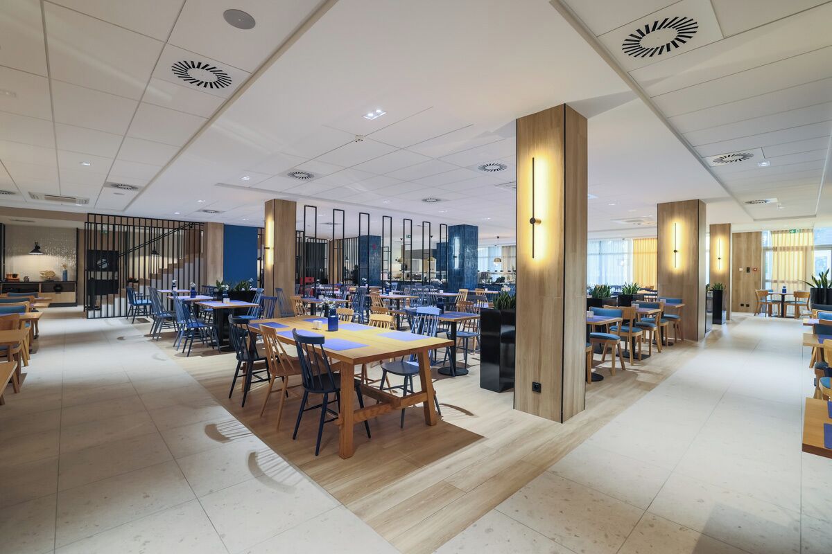 A spacious hotel lobby with multiple seating areas, including tables and chairs, and a central column with a light fixture.