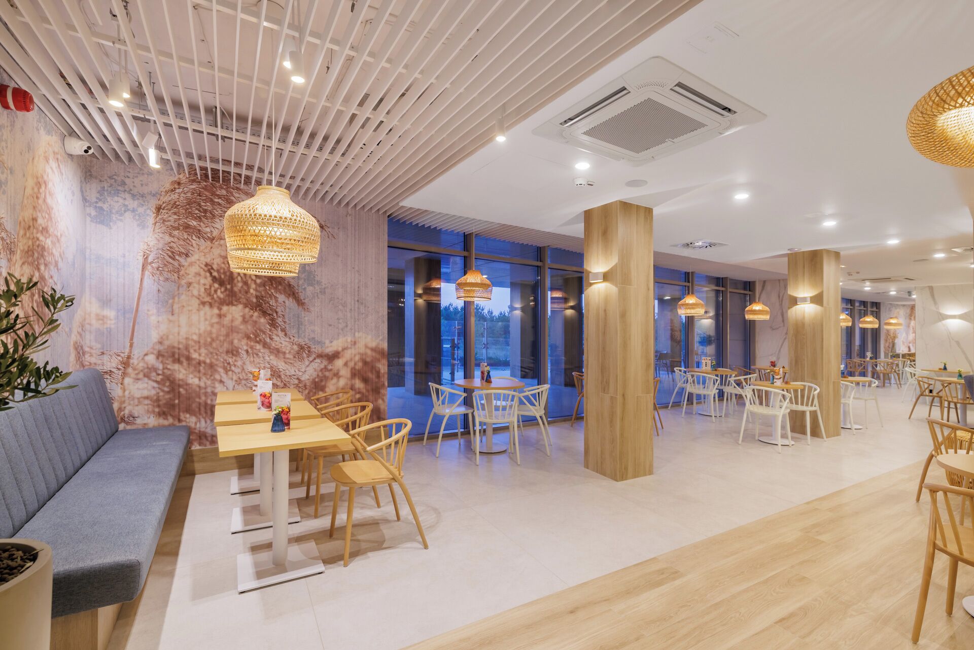 Un interior de restaurante moderno con mesas y sillas de madera, ventanas amplias e iluminación decorativa.