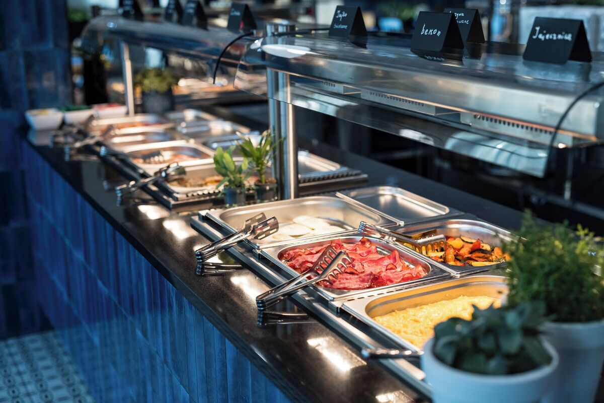 A buffet with various food options, including meats, vegetables, and other dishes, arranged on stainless steel serving trays.