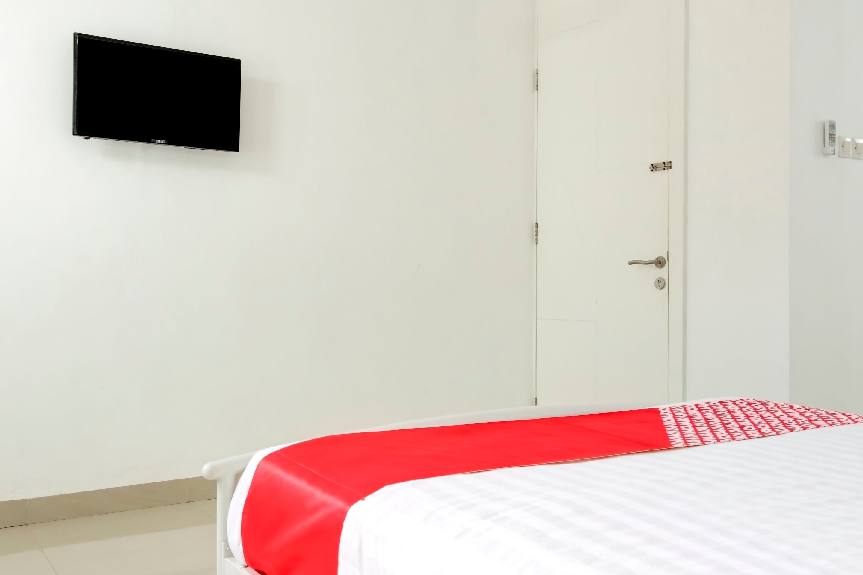 A bedroom with a bed, a television mounted on the wall, and a door.