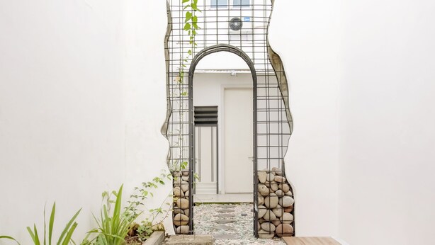 A narrow pathway leading to a door with a metal archway, surrounded by plants and pebbles. - Hotel O Panakkukang Near Mall Panakkukang Formerly Golden White House (Makassar)