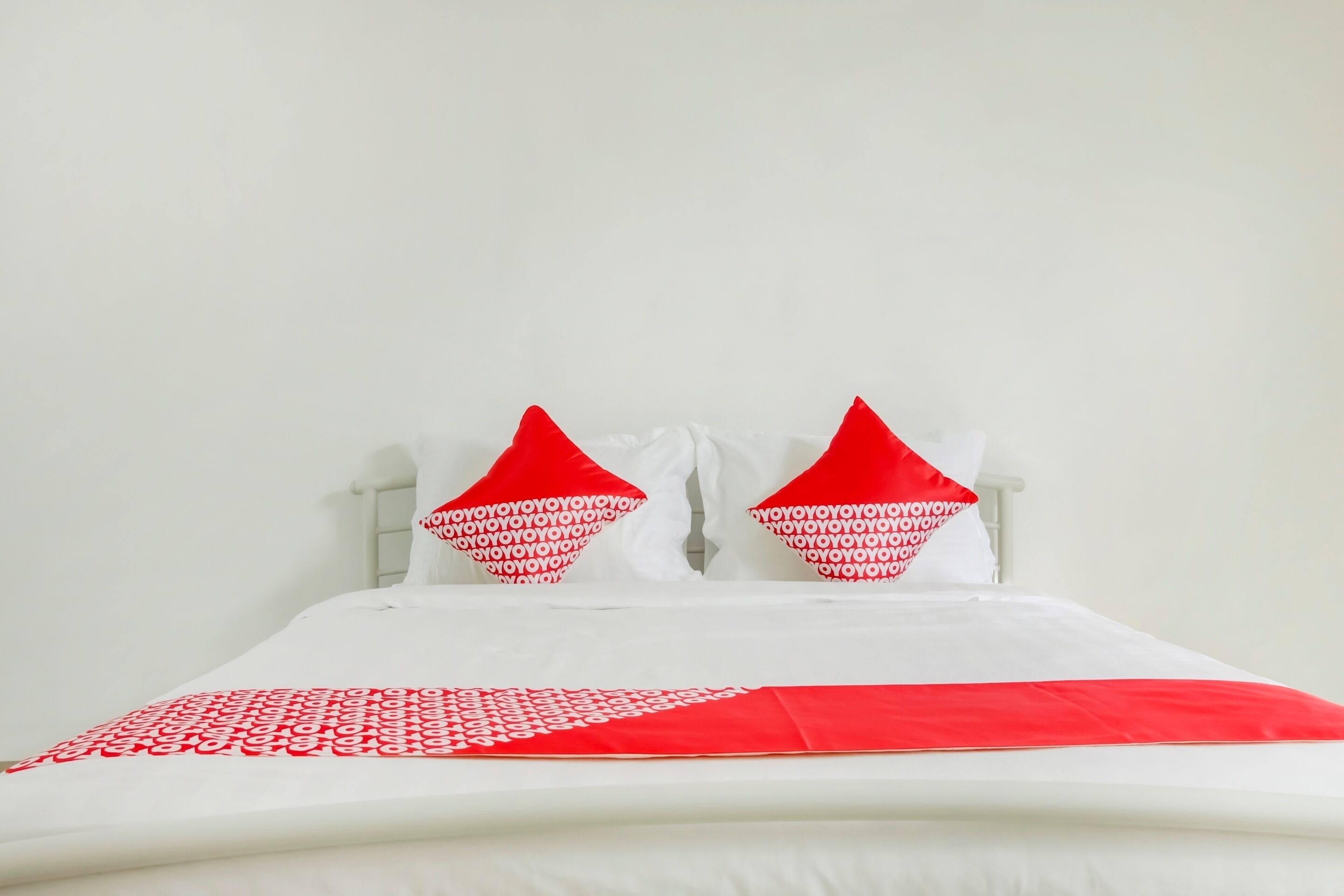 A bed with white bedding and two red pillows with a white pattern.