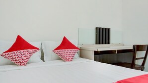 A hotel room with a bed, two red pillows with a repeating pattern, a white bedside table, a mirror, and a wooden chair. - Hotel O Panakkukang Near Mall Panakkukang Formerly Golden White House (Makassar)