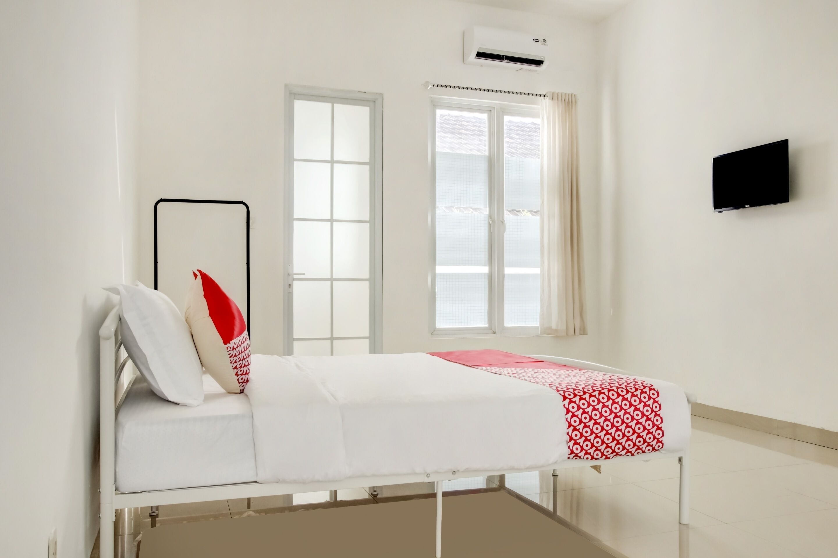 Une chambre d’hôpital avec un lit, des murs blancs, une fenêtre et un téléviseur fixé au mur.