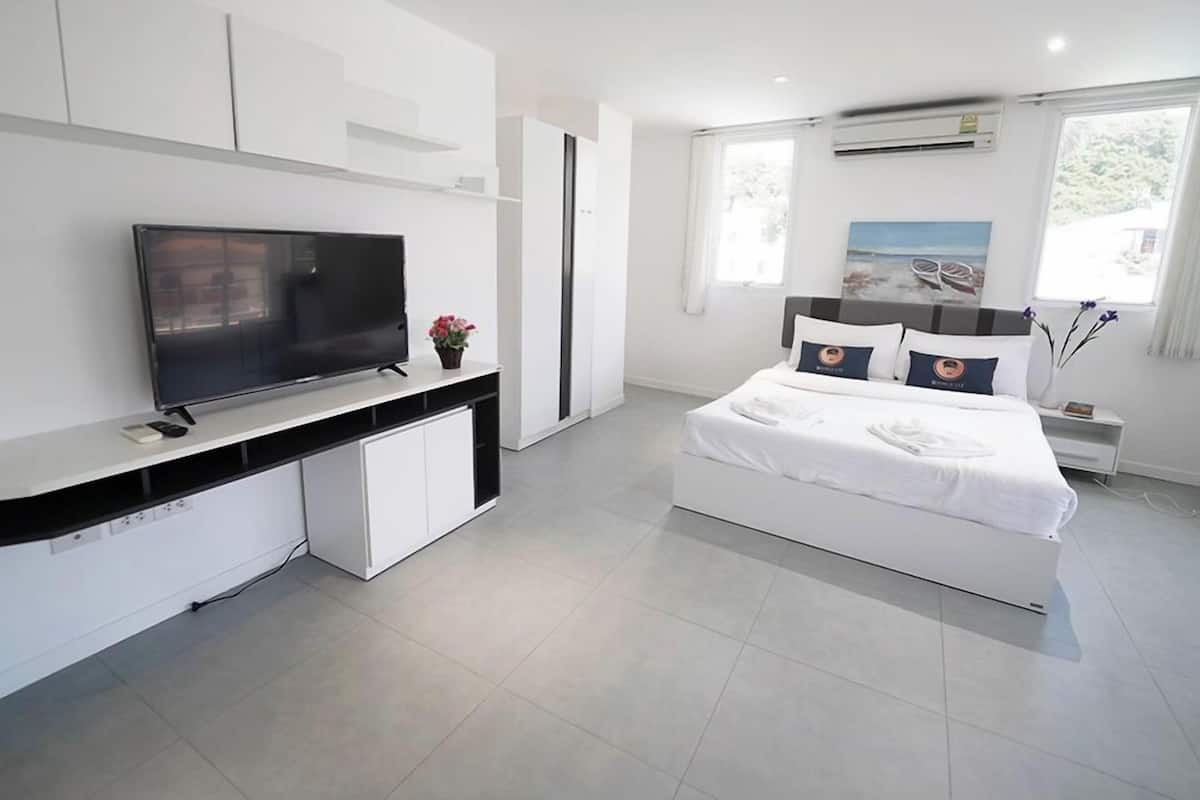 Une chambre d’hôtel moderne avec un grand lit, un téléviseur posé sur une console blanche et une fenêtre donnant sur la mer.