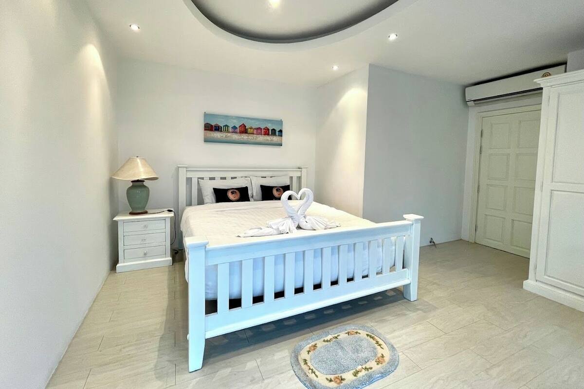 Une chambre à coucher avec un lit blanc, une table de chevet, une lampe, un tableau et une armoire.