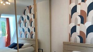 Une chambre avec un grand miroir, deux lits, une table de chevet et un mur orné d’un motif géométrique.
