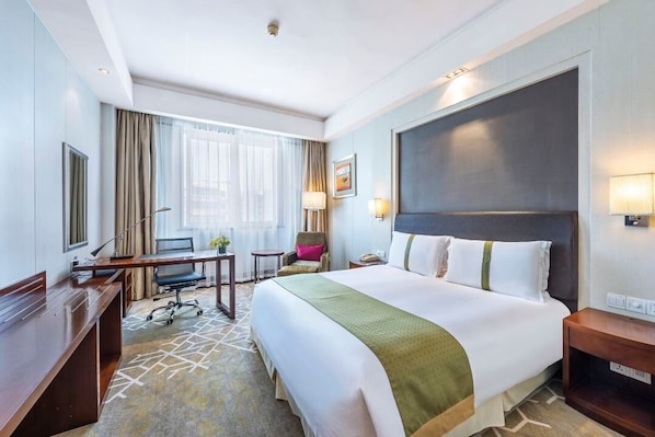Une chambre d’hôtel avec un grand lit, un bureau, une chaise, une petite table et une fenêtre avec des rideaux.